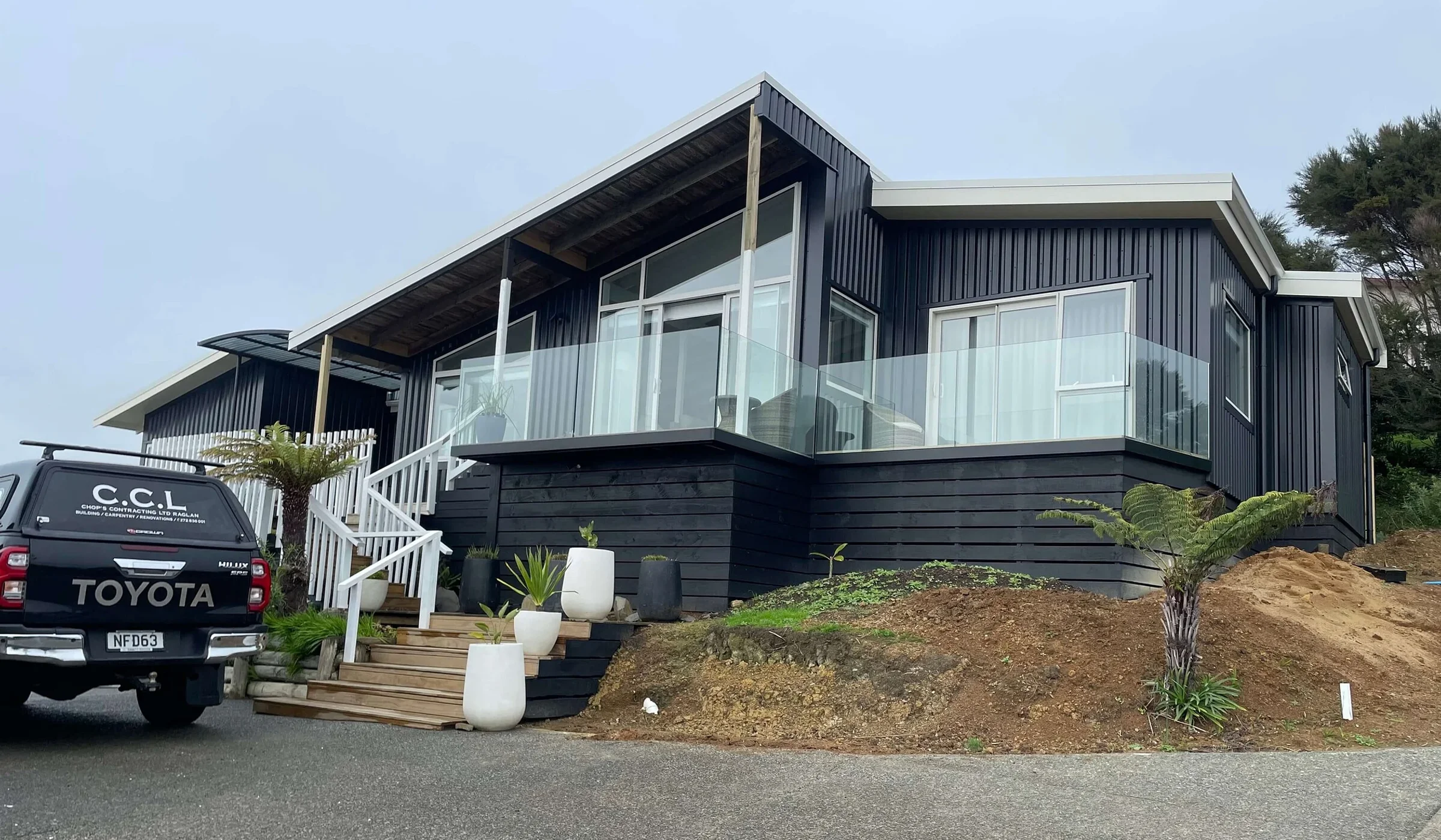 A completed Chops Contracting home in Raglan with dark vertical cladding and a glass-balustrade deck