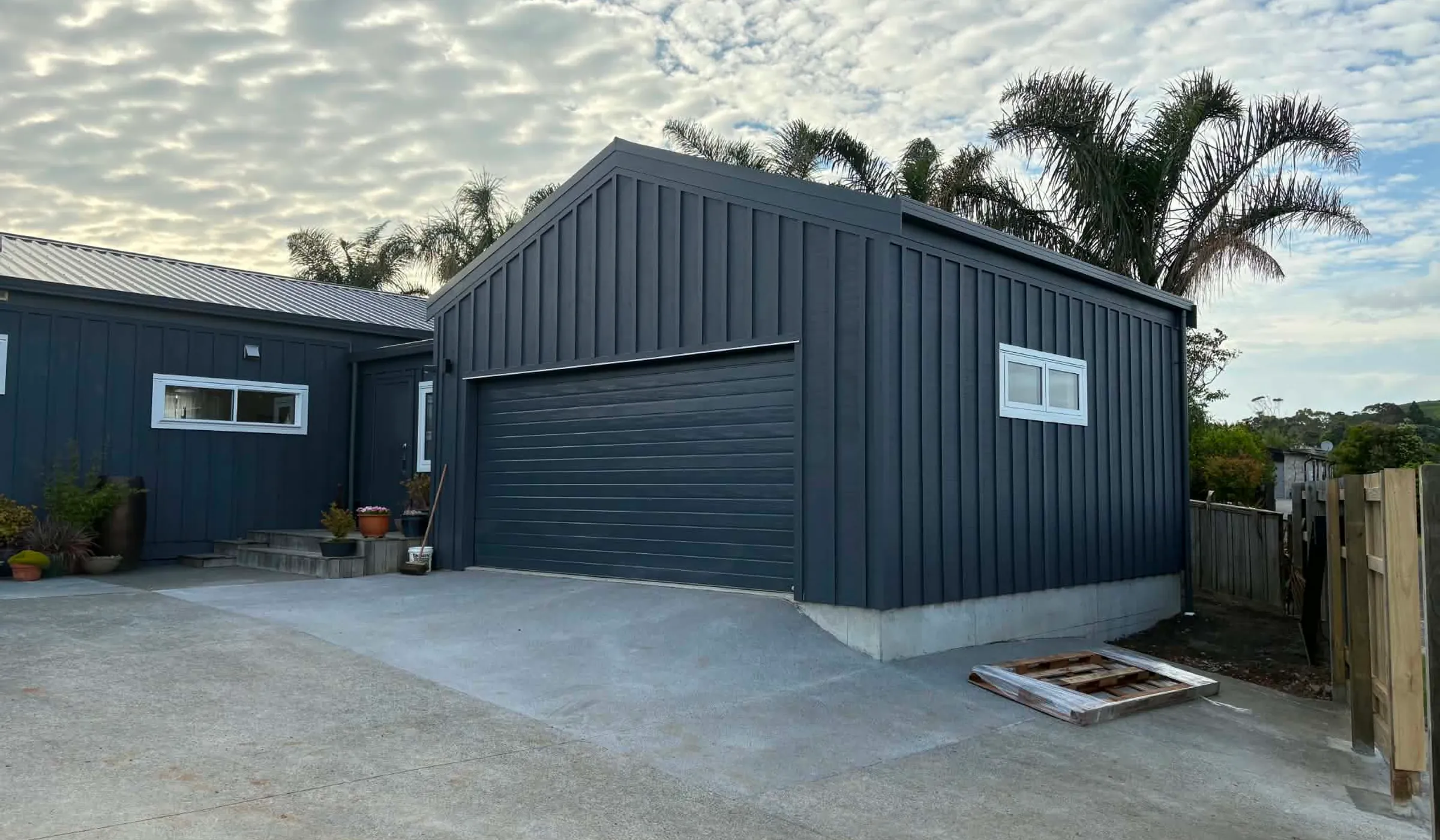 Finished double garage at Sunshine Rise, with the same dark vertical cladding and roof pitch as the original house at left
