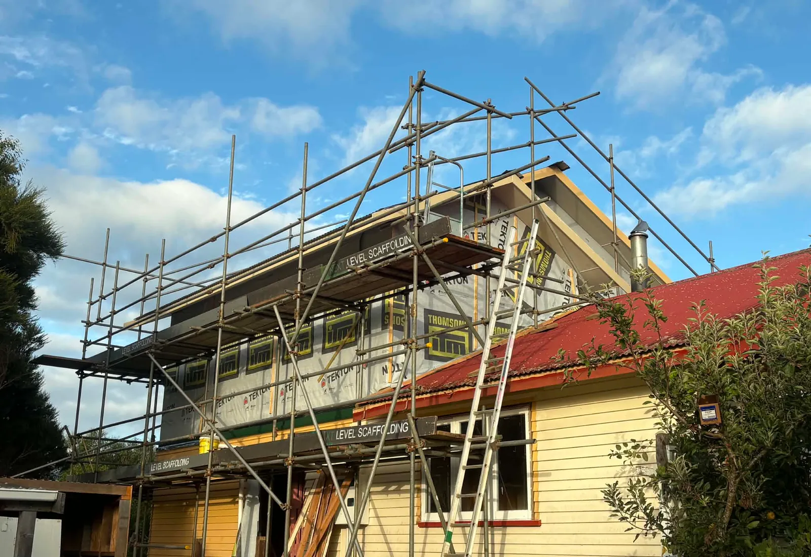 Scaffolded exterior with the new second storey wrapped and ready for cladding, original house roof at right