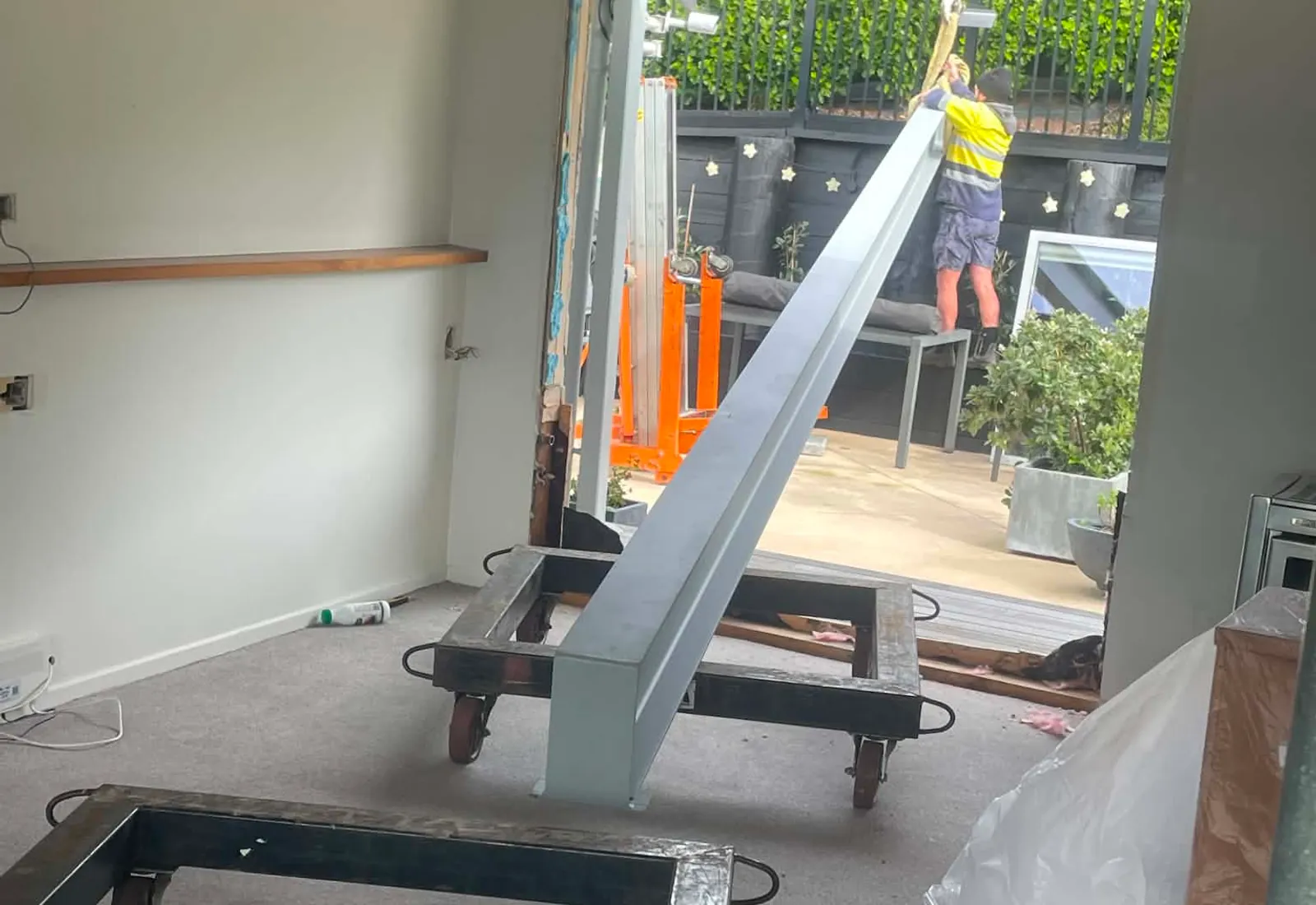 The 9-metre steel beam being lifted into the lounge through the open door, with heavy-duty trolleys waiting to take the load