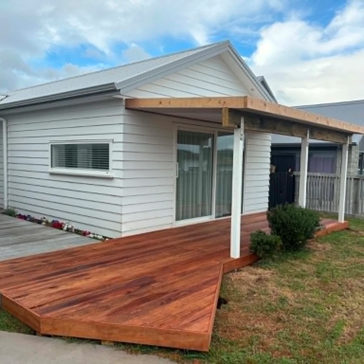 Finished freshly-oiled hardwood deck with a small porch roof, attached to a white weatherboard Raglan home