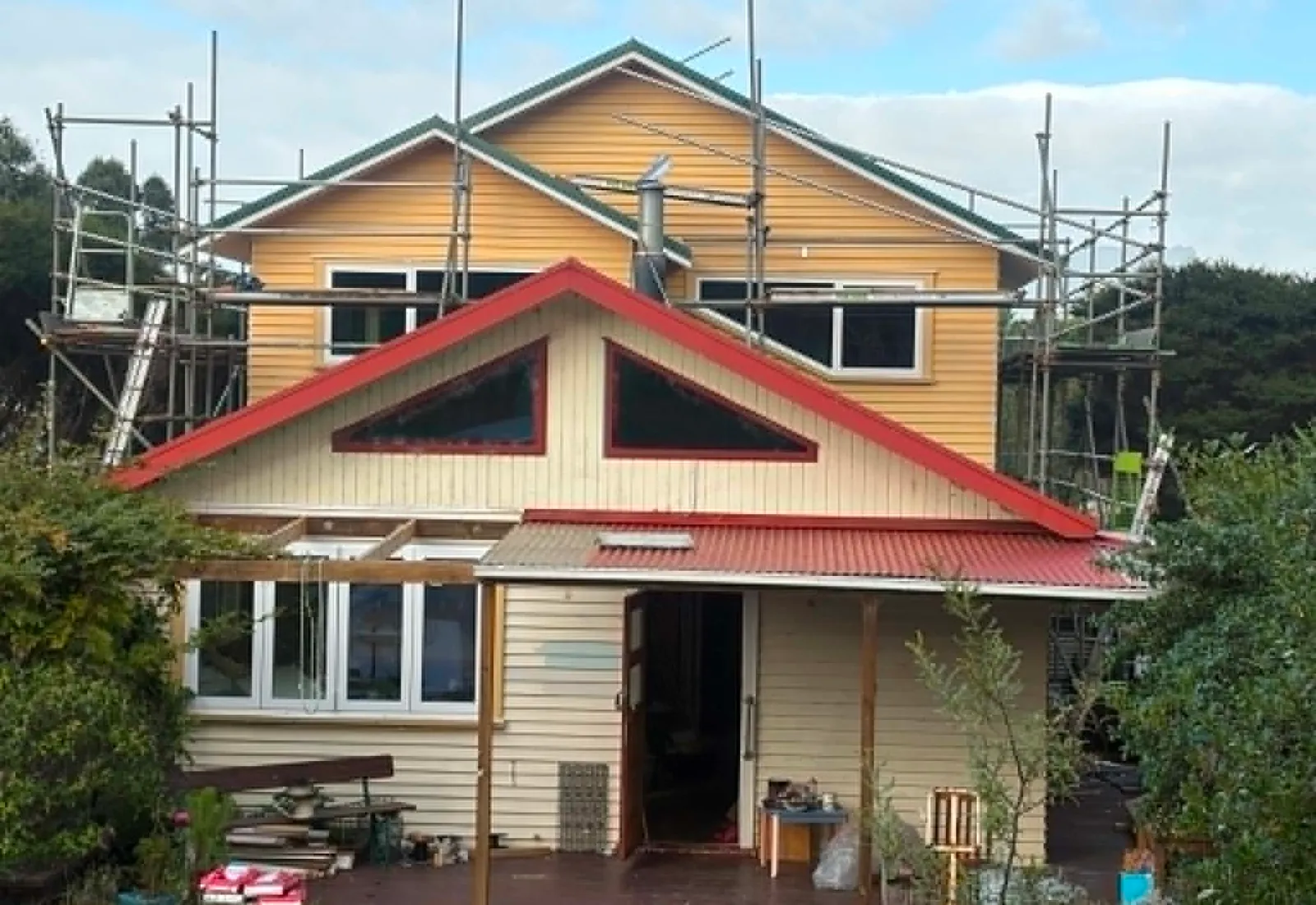 Mid-build view of a two-storey addition on a Raglan home, with the original red-roof single-storey wing visible below and the new upper level scaffolded for finishing