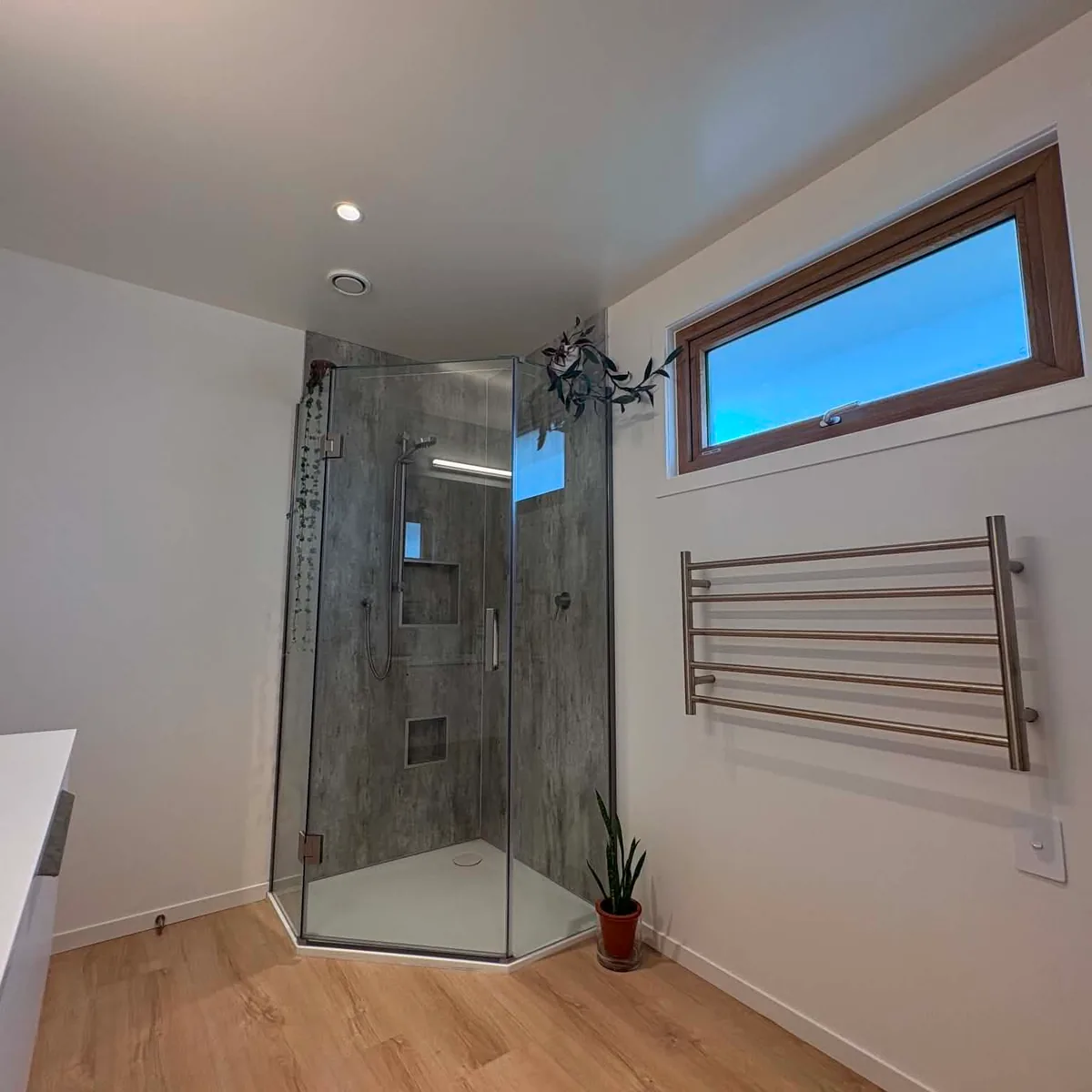 Finished bathroom with a corner glass shower, stone-look tile, towel rail and timber floor