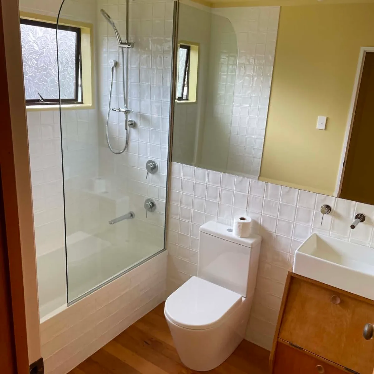 Renovated bathroom with white square tile, glass shower screen, timber vanity and timber floor