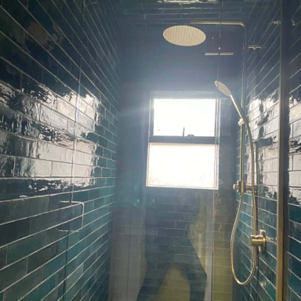 Walk-in shower with deep teal subway tile, rainfall showerhead and brass fittings